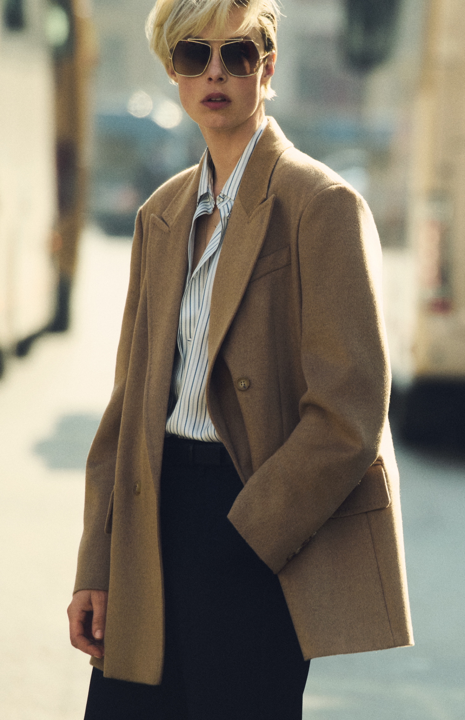 Das Model trägt den doppelreihigen Blazer Olimpia von Max Mara im Farbton Kamel zu dunkler Brille und Bluse im urbanen Kontext.