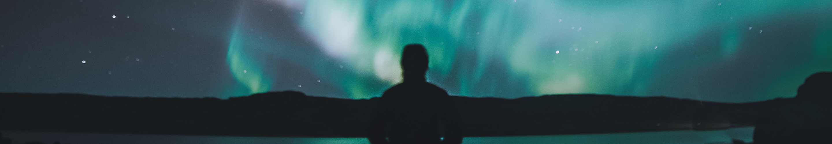 Silhouette of a person standing in a mountain landscape at night and admiring the aurora borealis.