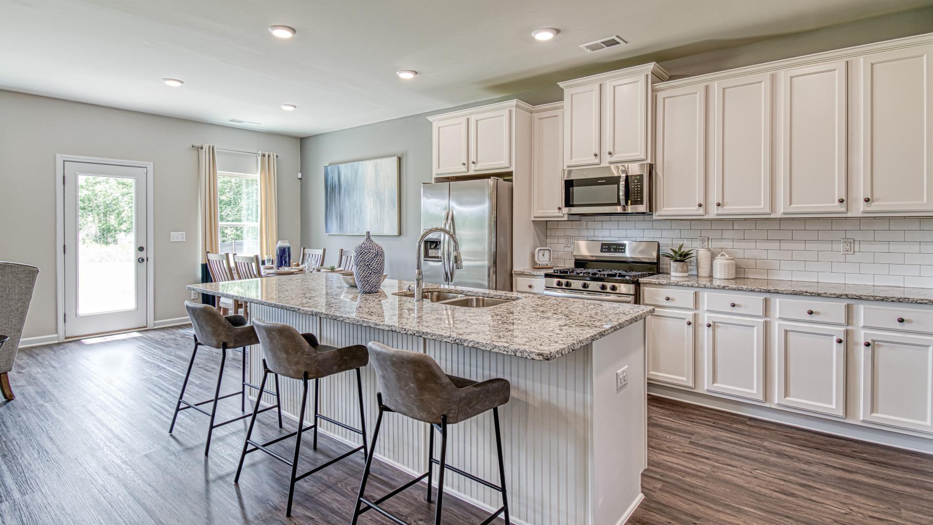 Kitchen with white cabinets and island with 3 bar stools in the DRB Homes Traditions at Crystal Lake community