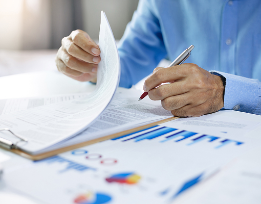 Man writing on one of several documents splayed in front of him on a table.