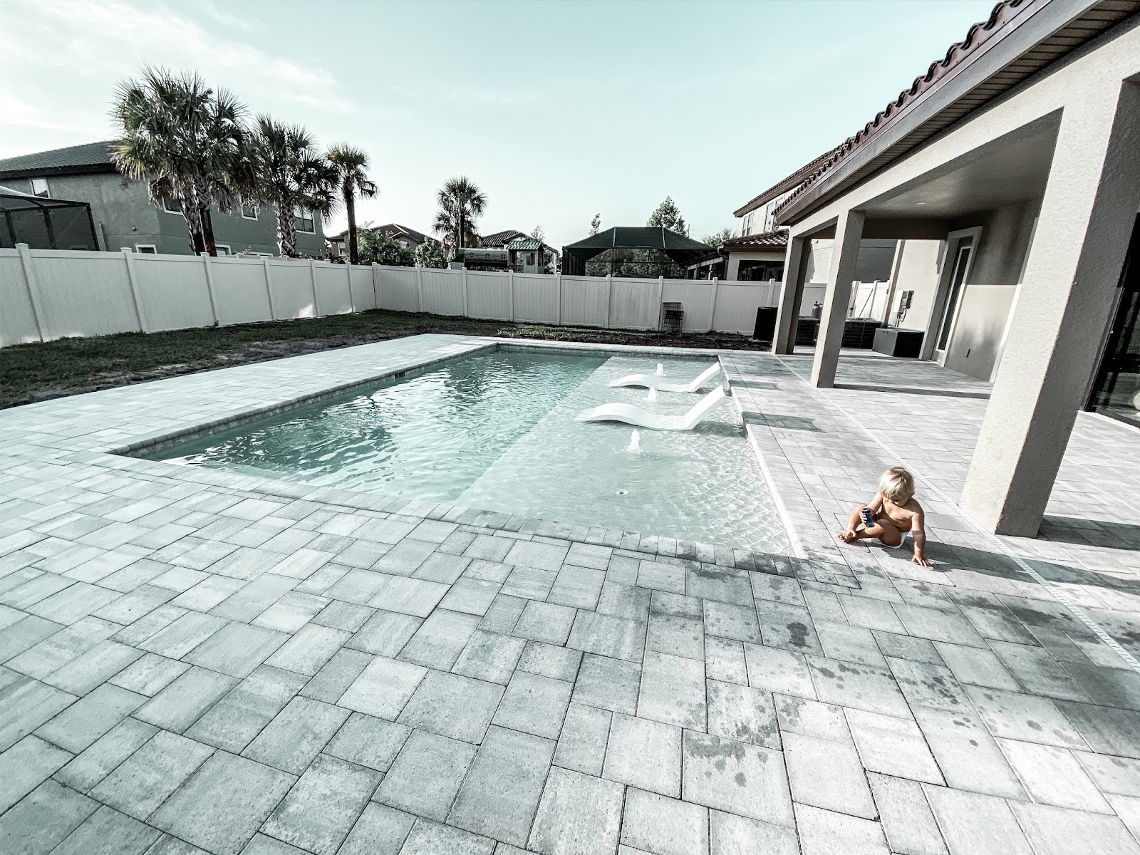 Contemporary backyard swimming pool with light paver decking, a covered patio, and a spacious private residential setting.
