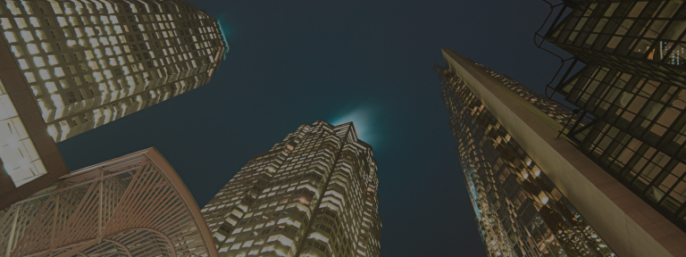 Upward view of several large skyscrapers at night.