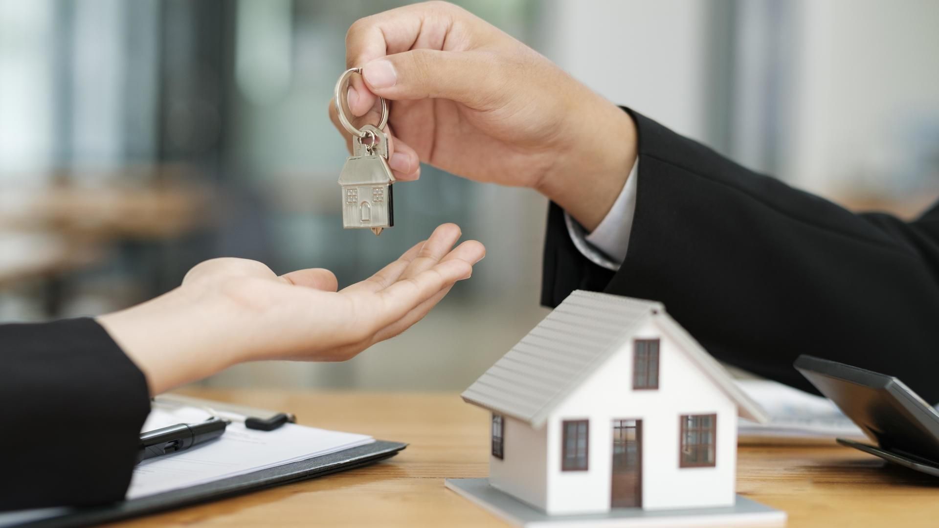Real estate agent handing over house keys to a new homeowner during a property transaction meeting. The image represents successful home buying, property management services, real estate investment opportunities, and professional customer-focused residential sales assistance for buyers and investors.