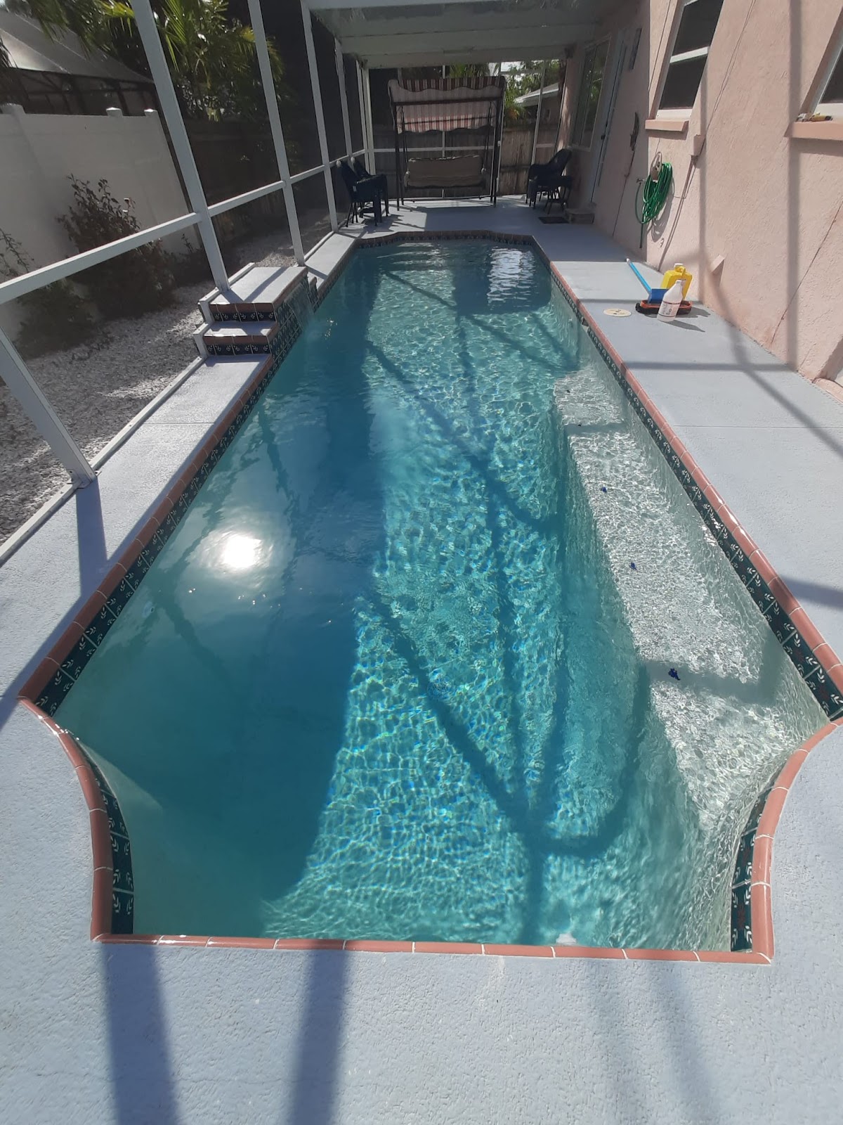 Long narrow residential swimming pool inside a screened enclosure, with clear water and a simple pool deck.