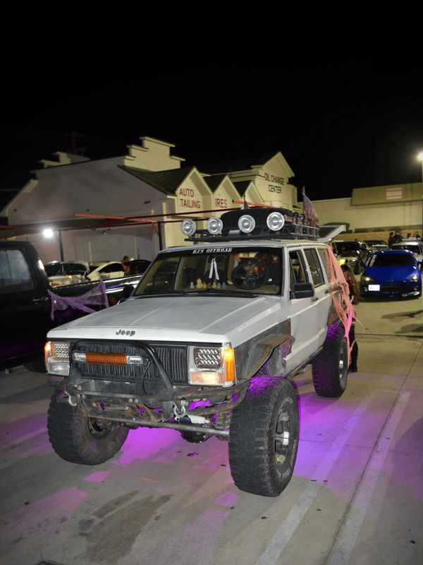 Lifted white Jeep Cherokee displayed at a nighttime automotive gathering outside an oil change cente 