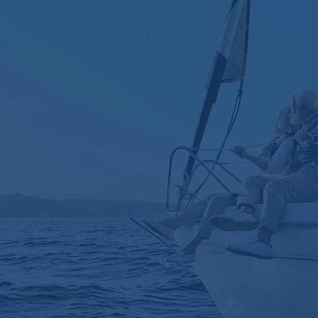 An elderly couple sitting on the bow of a boat with their legs hanging down.