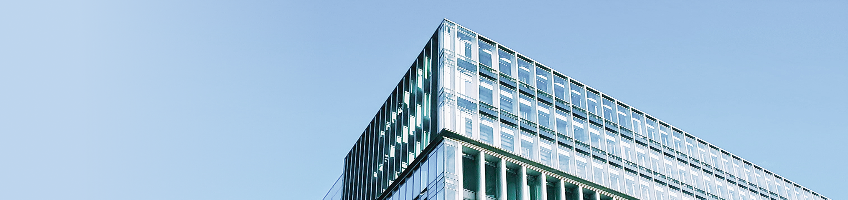 The top of a modern glass office building against a clear blue sky.