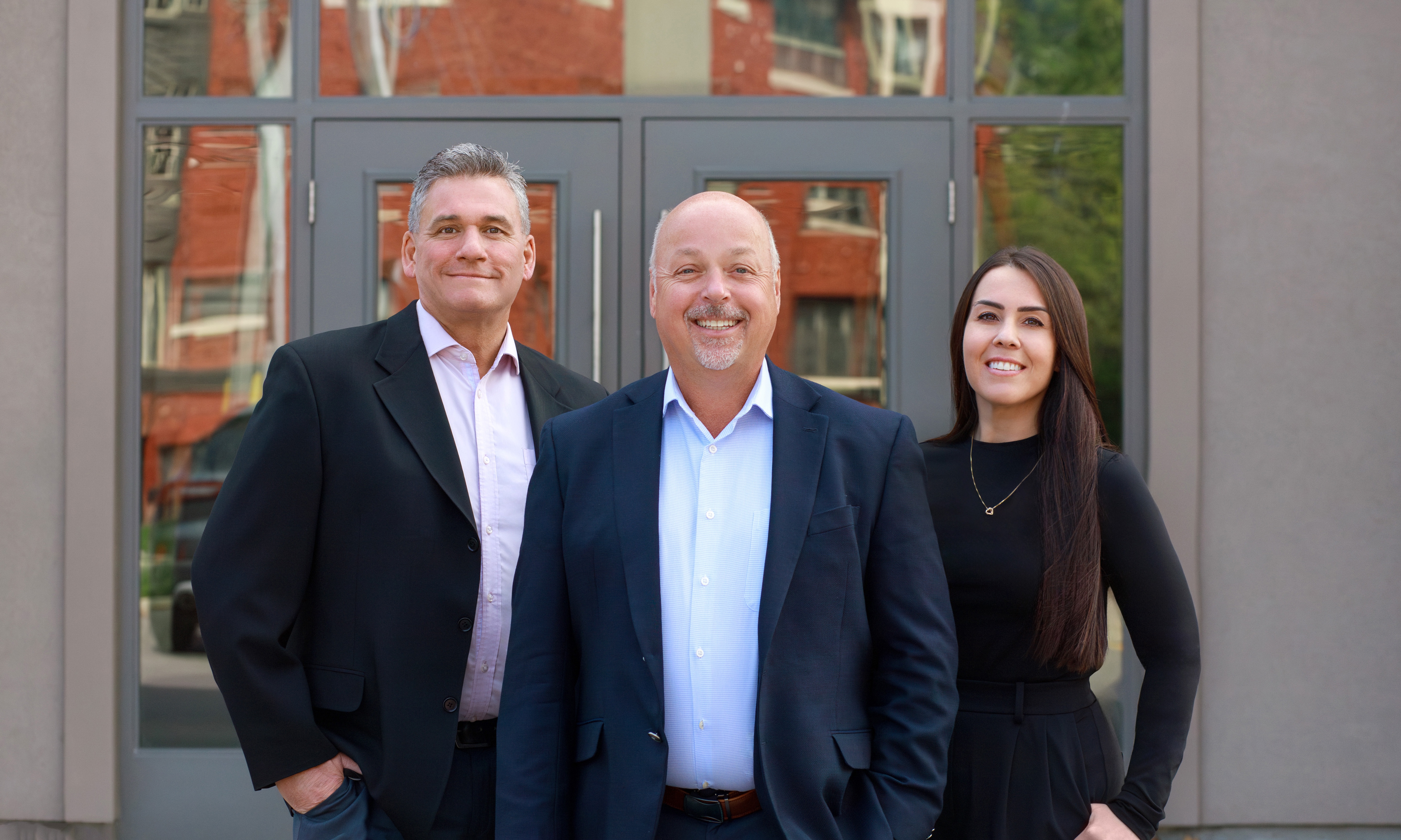 Team photo of Robert Corchis, Jeff Utley, and Ashleigh Deacon, stand outside their office building.