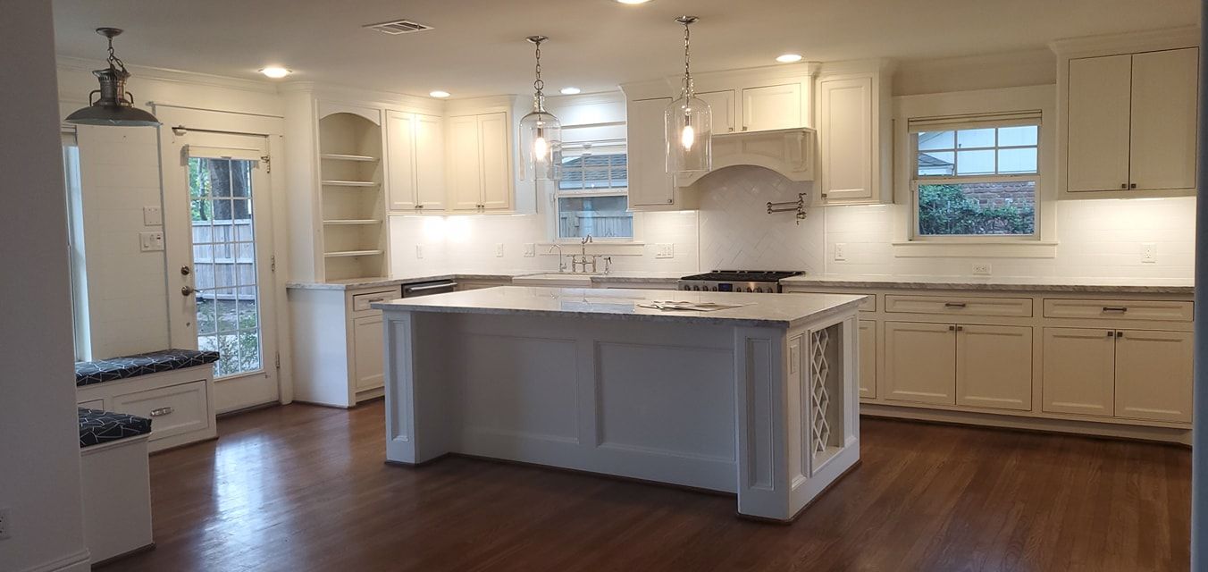 Freshly painted white kitchen featuring custom cabinetry, oversized island, elegant pendant lighting, hardwood floors, and bright finishes creating a timeless, spacious, and sophisticated cooking and gathering environment.