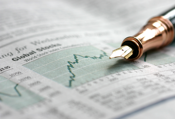 A close-up of a pen laying on stop of a printed stock chart.