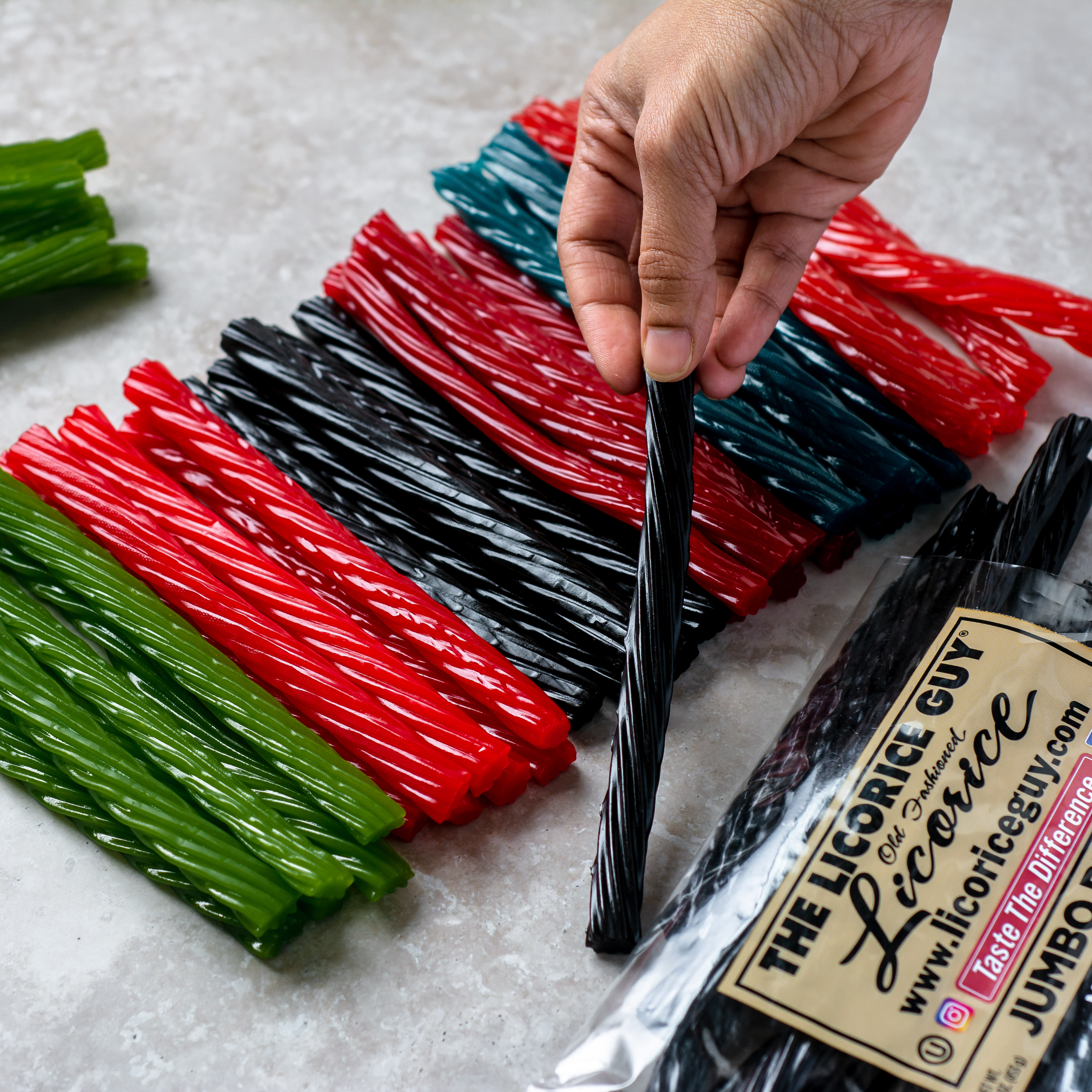 A colorful array of The Licorice Guy's old fashioned licorice flavors, including green apple, traditional red, traditional black, and blue raspberry, displayed alongside branded packaging.