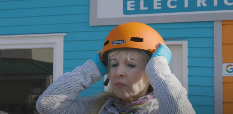 A woman adjusts a bright orange bike helmet.