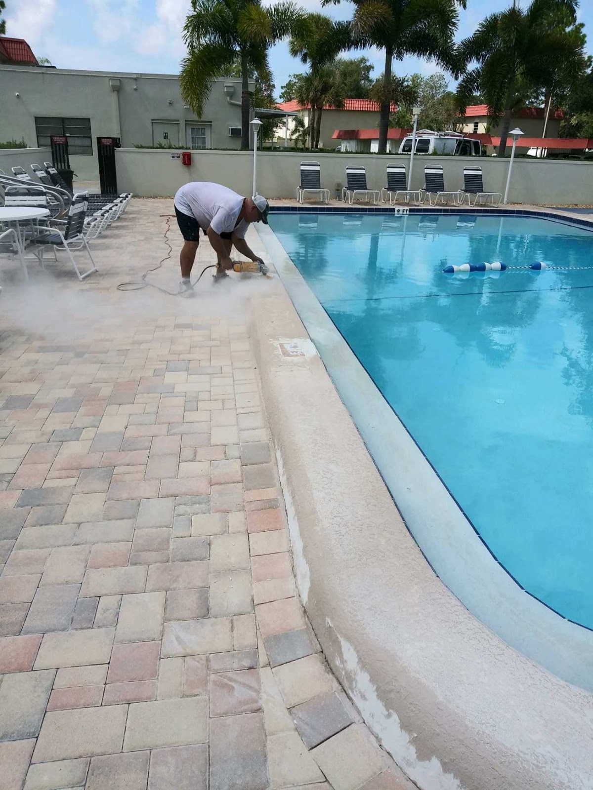 Large community swimming pool with clear blue water, paver decking, and a pool service professional working along the pool edge.