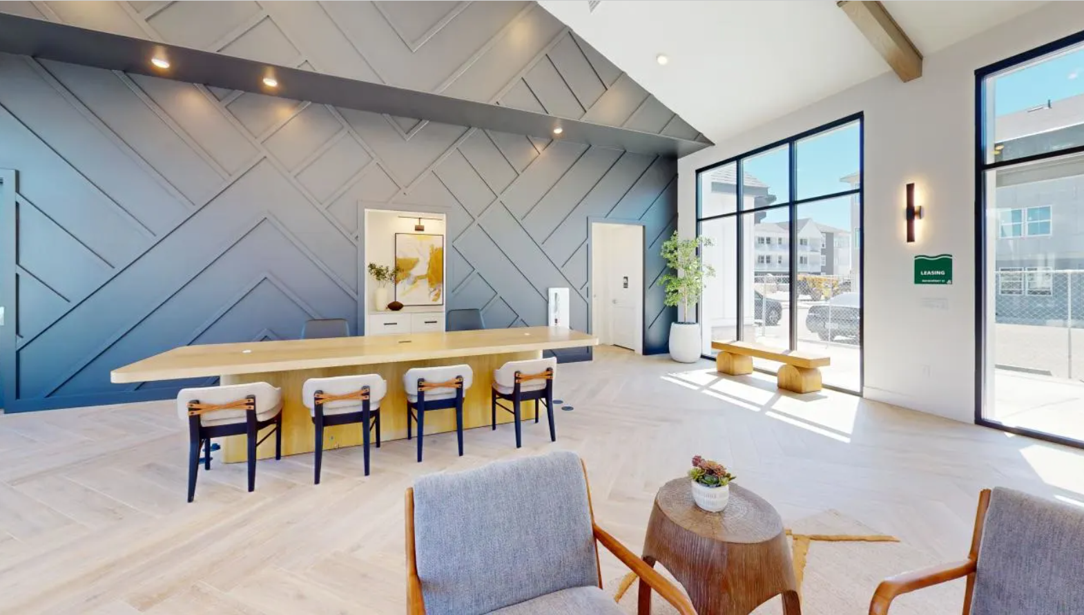 Spacious resident seating area with a wooden table and cozy chairs, perfect for working from home, completed by oversized windows and a navy patterned wall design