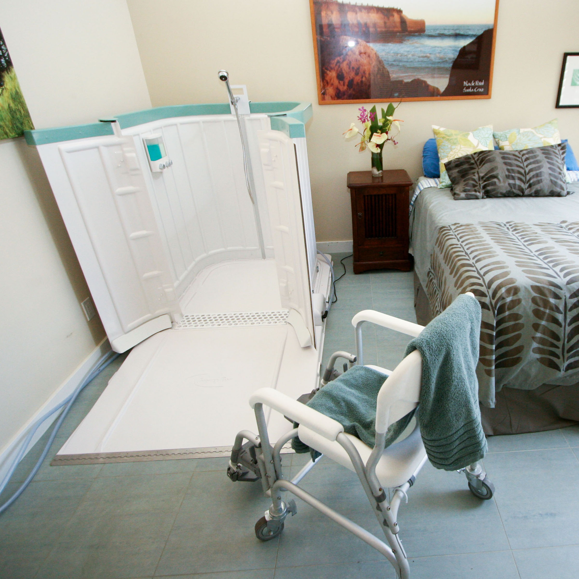 Shower Bay portable shower positioned beside a bed with an accessibility chair, making bathing easier for seniors, patients, and caregivers.