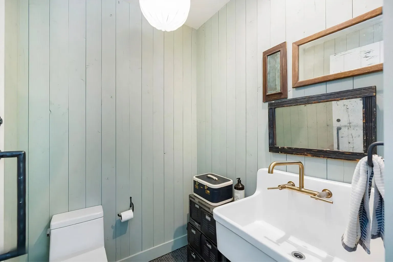Charming powder room featuring paneled walls, farmhouse sink, and vintage-inspired accents. Custom design combines rustic character with modern convenience and efficient use of space.