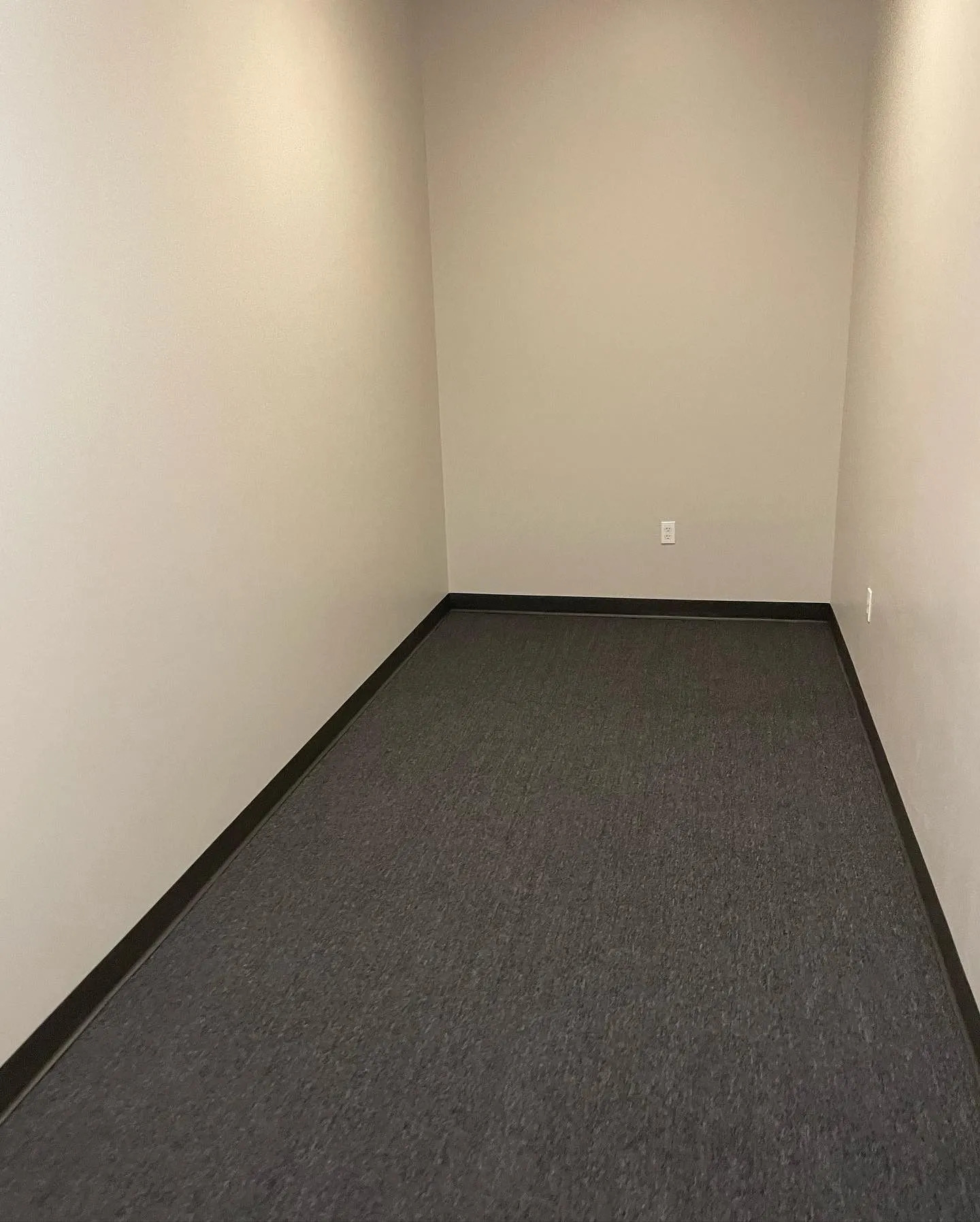 Finished office room with freshly painted neutral walls, commercial carpet flooring, black baseboard 
