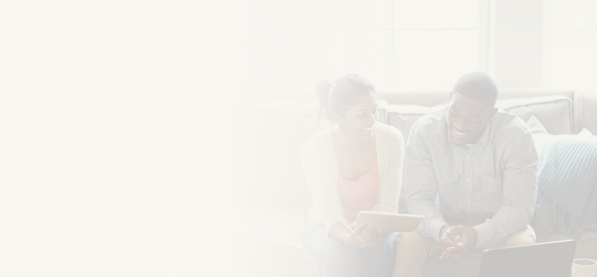 A smiling young couple sitting on their couch reviewing documents together.