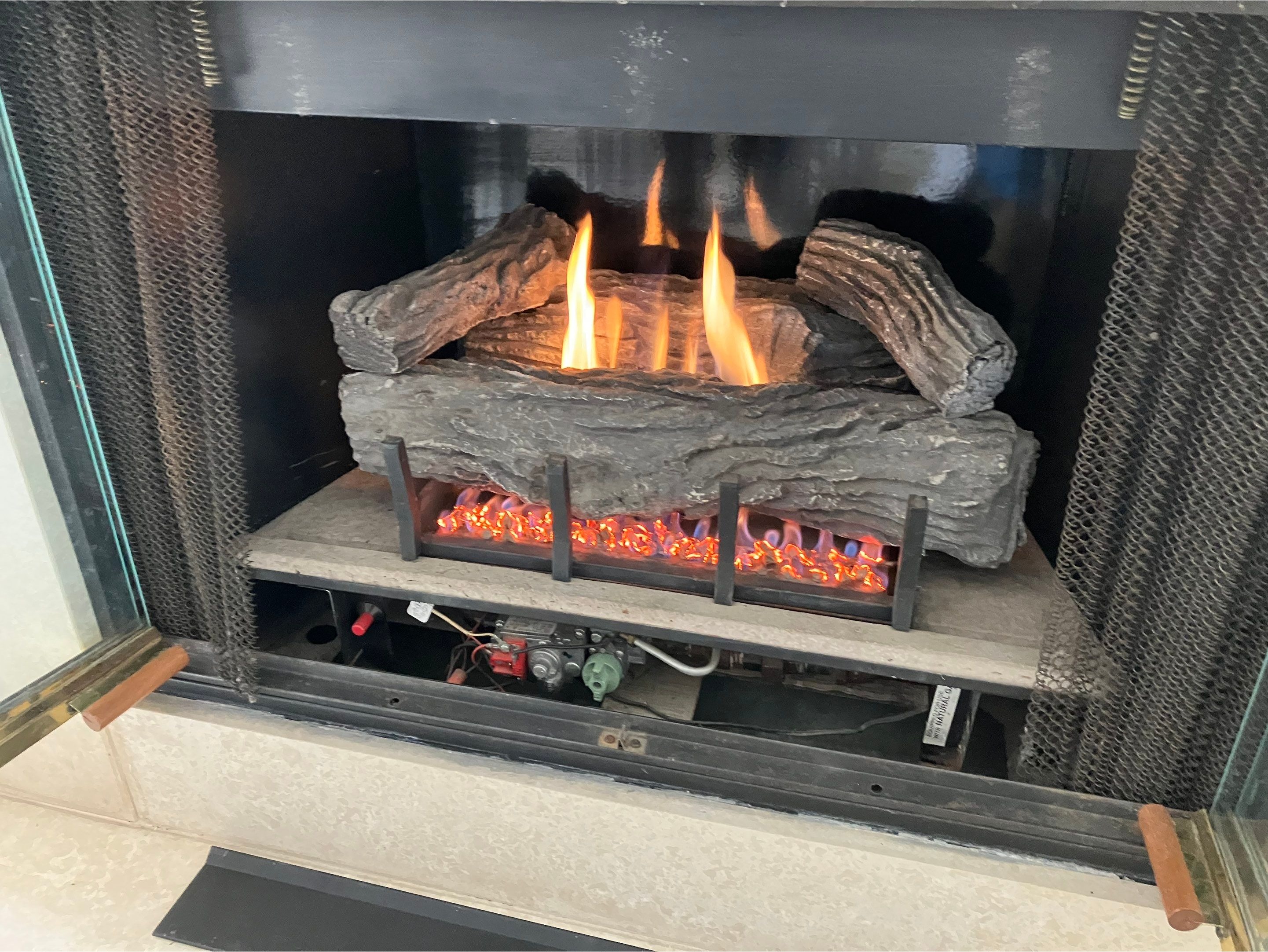 Gas log set burning with tall flames and a glowing ember bed during a gas fireplace repair and diagn 