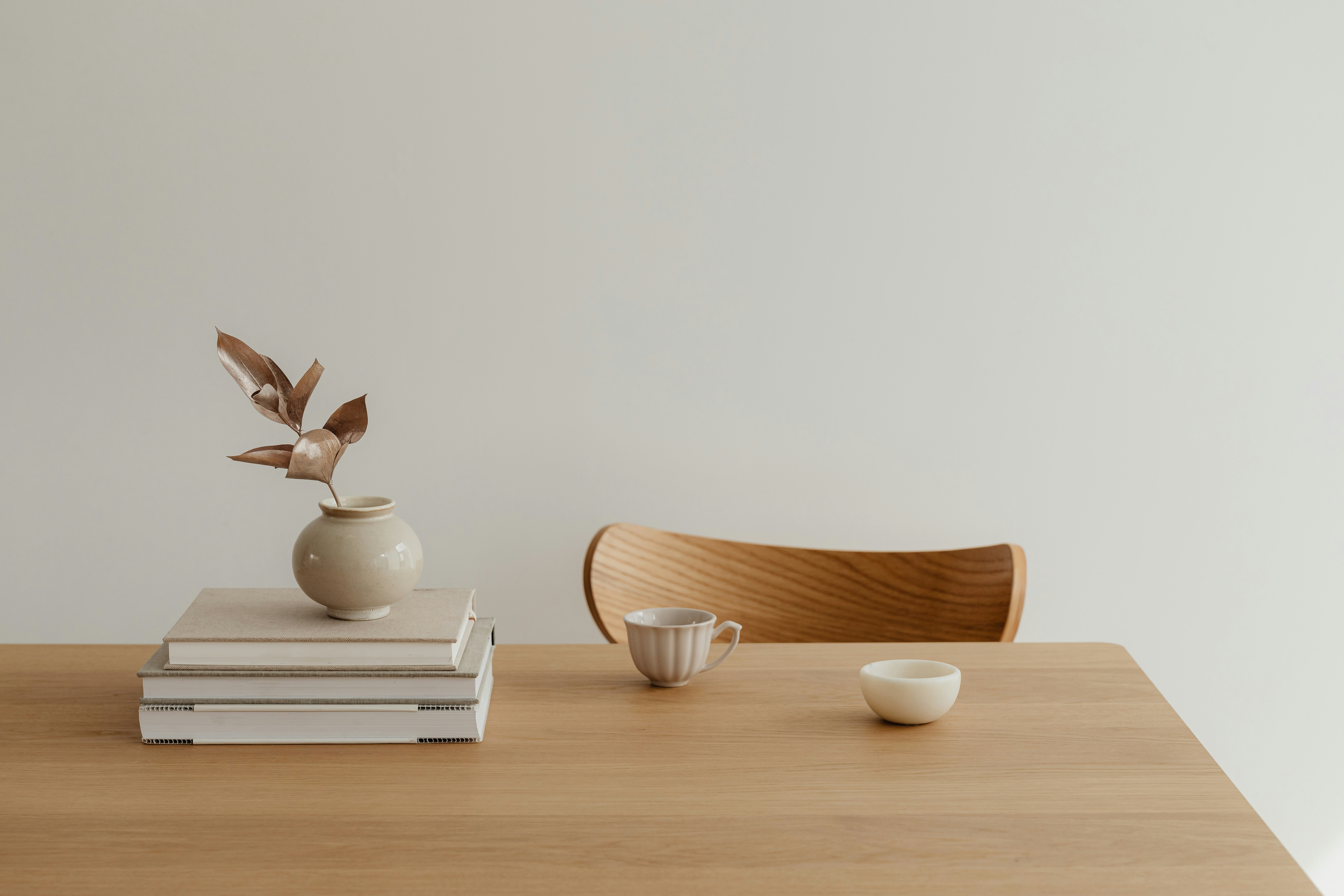 A table with a stack of books, tea cup and chair.