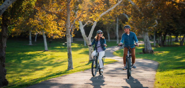 A man and a woman riding on their Pedego electric bikes through a park