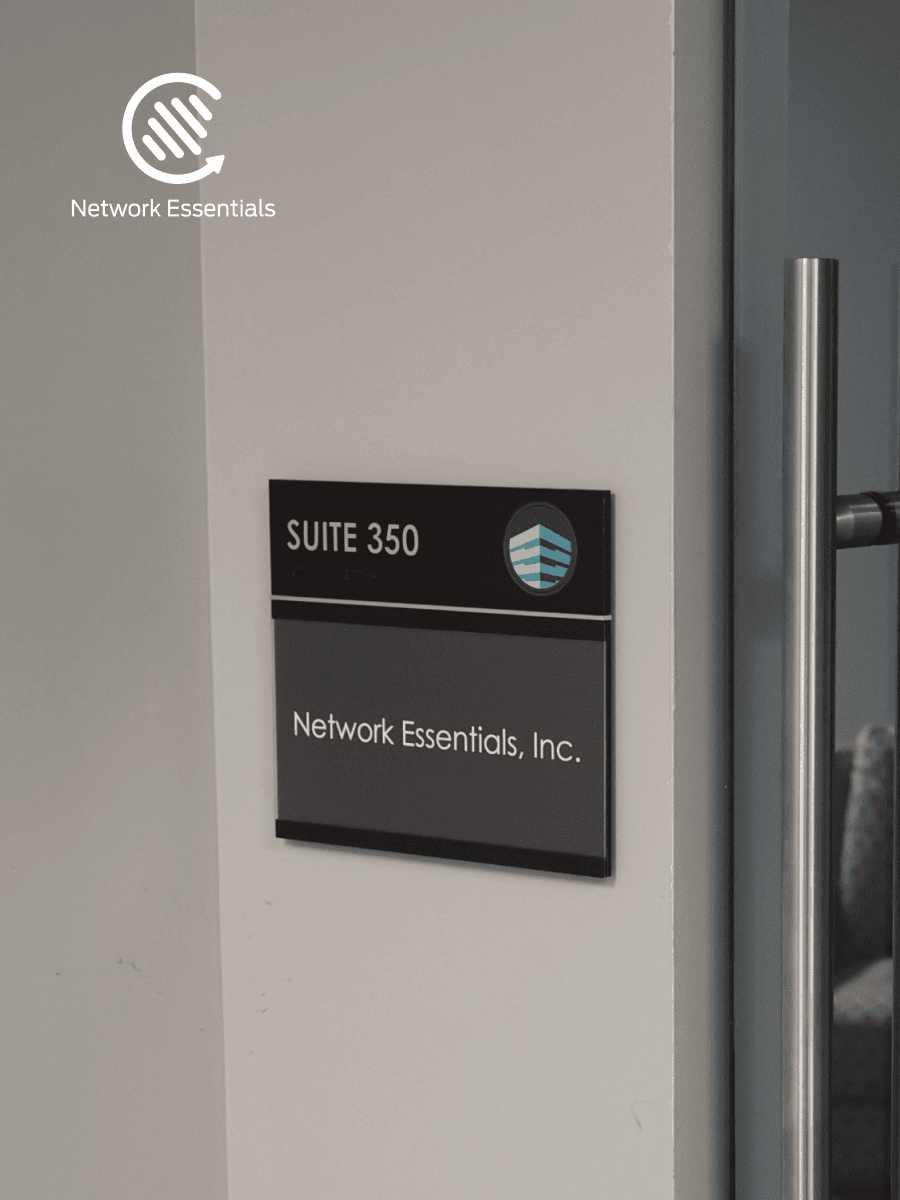 A dark gray sign with white text reads "SUITE 350" and "Network Essentials, Inc.". A logo is displayed to the right of "SUITE 350" which features blue and white horizontal lines within a circular frame. Above the sign, a white logo is visible on a light gray wall with the text "Network Essentials" below it. A silver door handle is visible on the right side of the image.