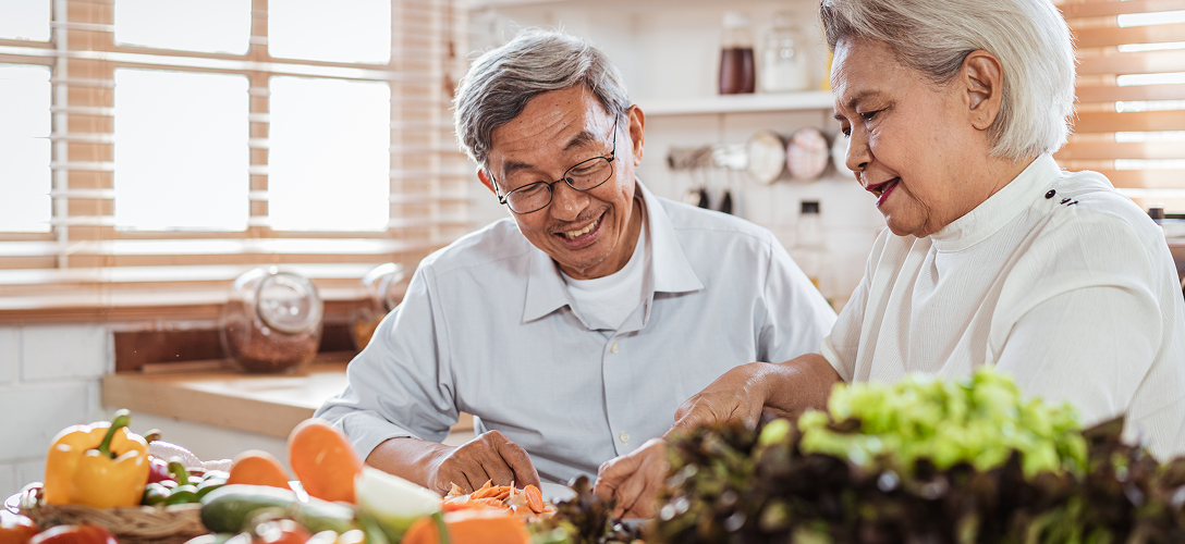 An elderly couple chopping vegetables together.