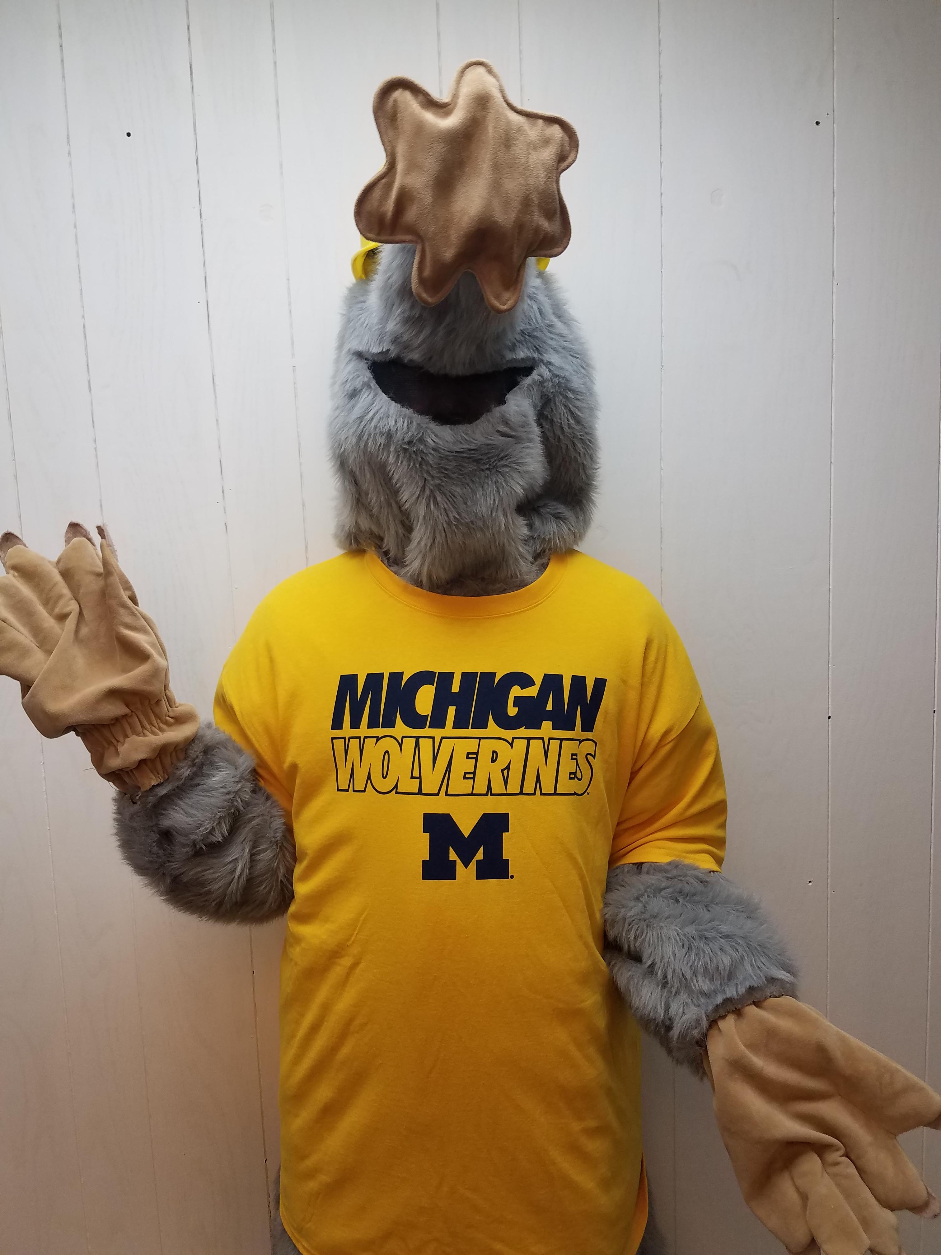 Mole mascot wearing a Michigan Wolverines tee-shirt and waving.