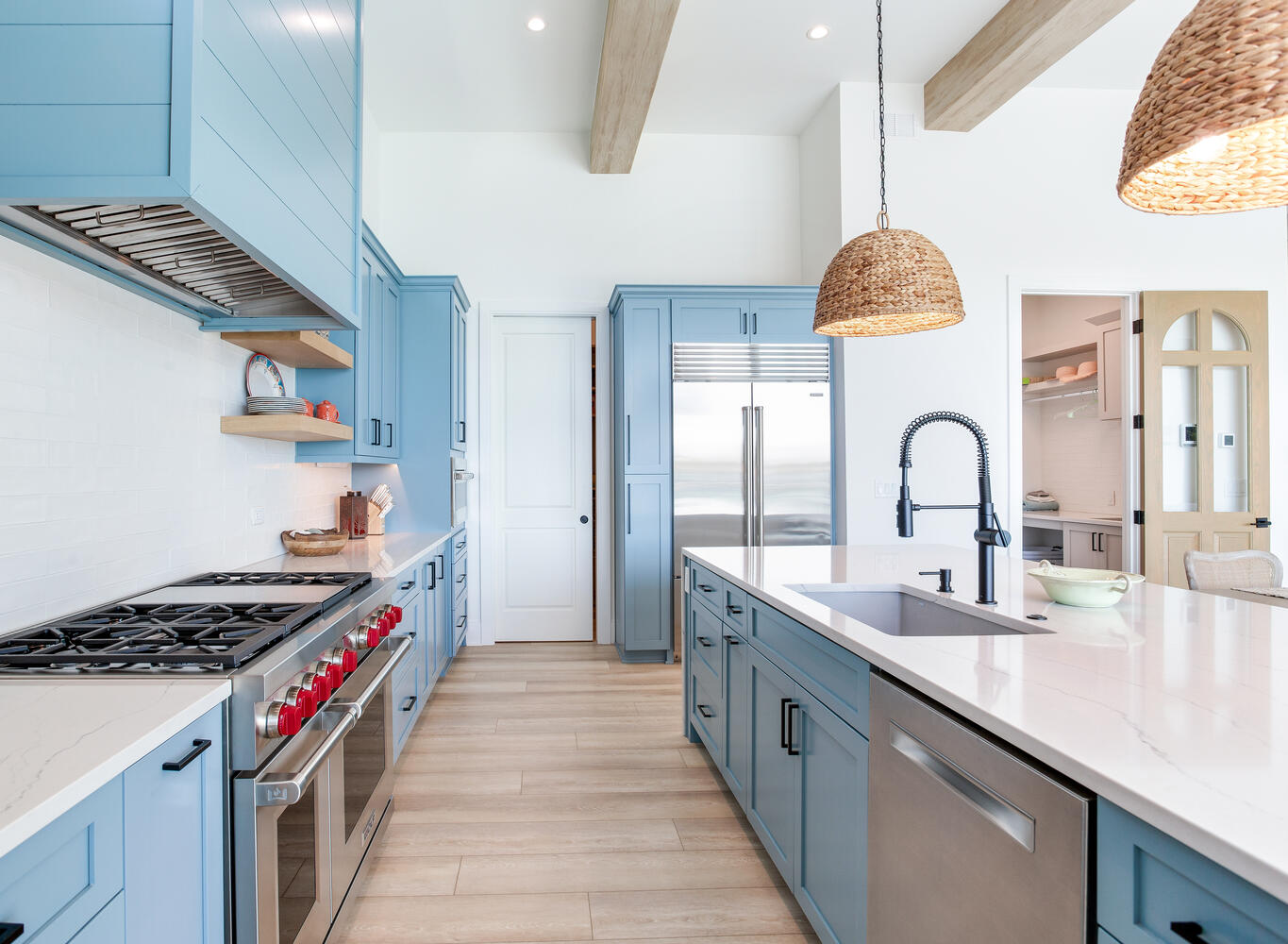 Luxury coastal kitchen with soft blue cabinetry, warm wood flooring, woven lighting, stainless appliances, and a clean custom design.