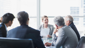 Professionals in grey suits engaged in light discussion in a meeting room.
