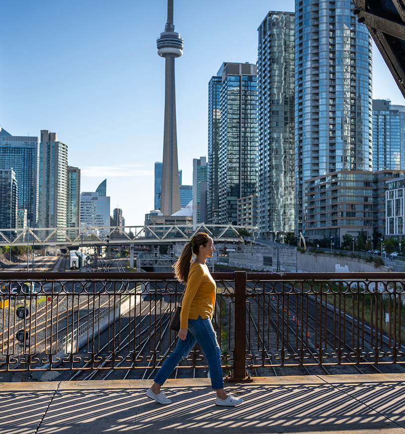 An individual walking along a bridge with the CN Tower in the background.