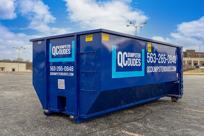 A blue QC Dumpster Dudes dumpster placed in an empty parking lot, ready for use in large-scale cleanouts or construction jobs.