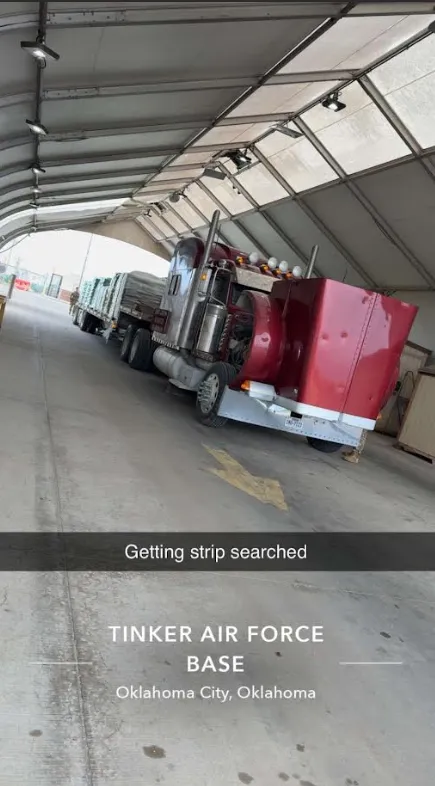 Red semi truck and flatbed trailer parked inside an inspection facility. Commercial freight vehicle undergoing security screening and compliance checks before continuing transportation operations and scheduled cargo delivery.