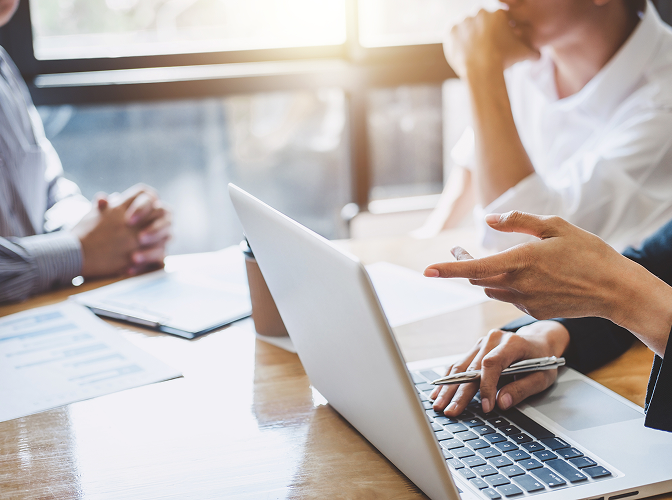 Close-up of three people sitting around a desk pointing at documents and a laptop.