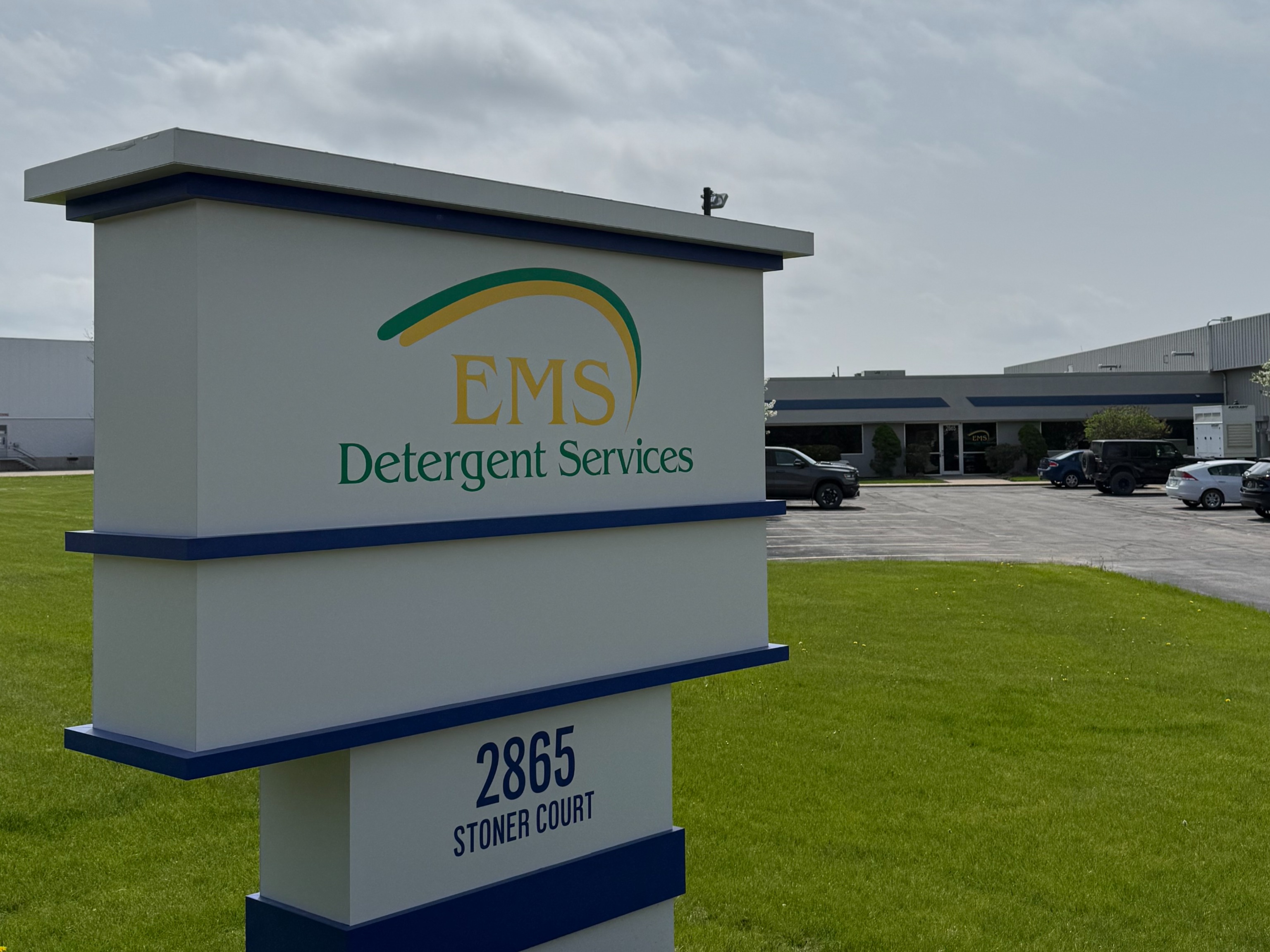 Exterior view of EMS Detergent Services at 2865 Stoner Court, featuring a branded monument sign on a landscaped lawn with the industrial facility and parking area in the background.
