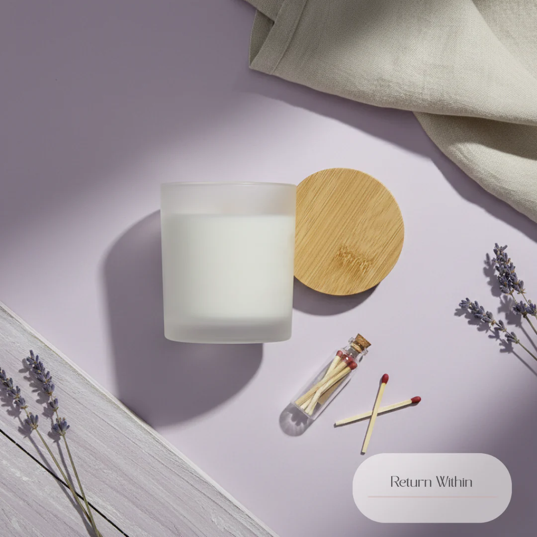 A top-down view of a frosted white candle in a glass jar with a bamboo lid sits on a lavender-colored surface, next to a small glass vial filled with matches and two loose matches. Dried lavender sprigs and a crumpled linen cloth are also visible. The scene is lit with dramatic shadows, and a text overlay reads 'Return Within'.