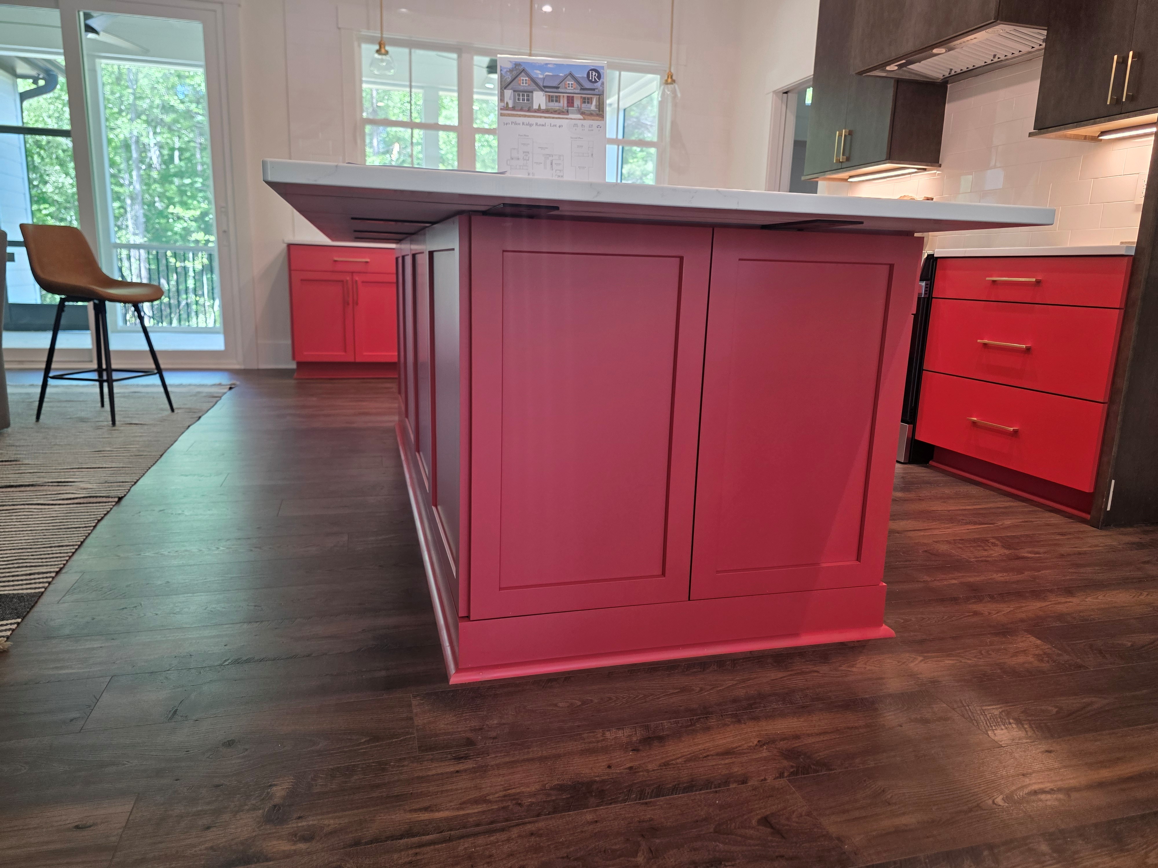 Close-up view of a custom red kitchen island with paneled cabinetry, white quartz countertop, and dark wood flooring, with natural light coming through nearby glass doors.