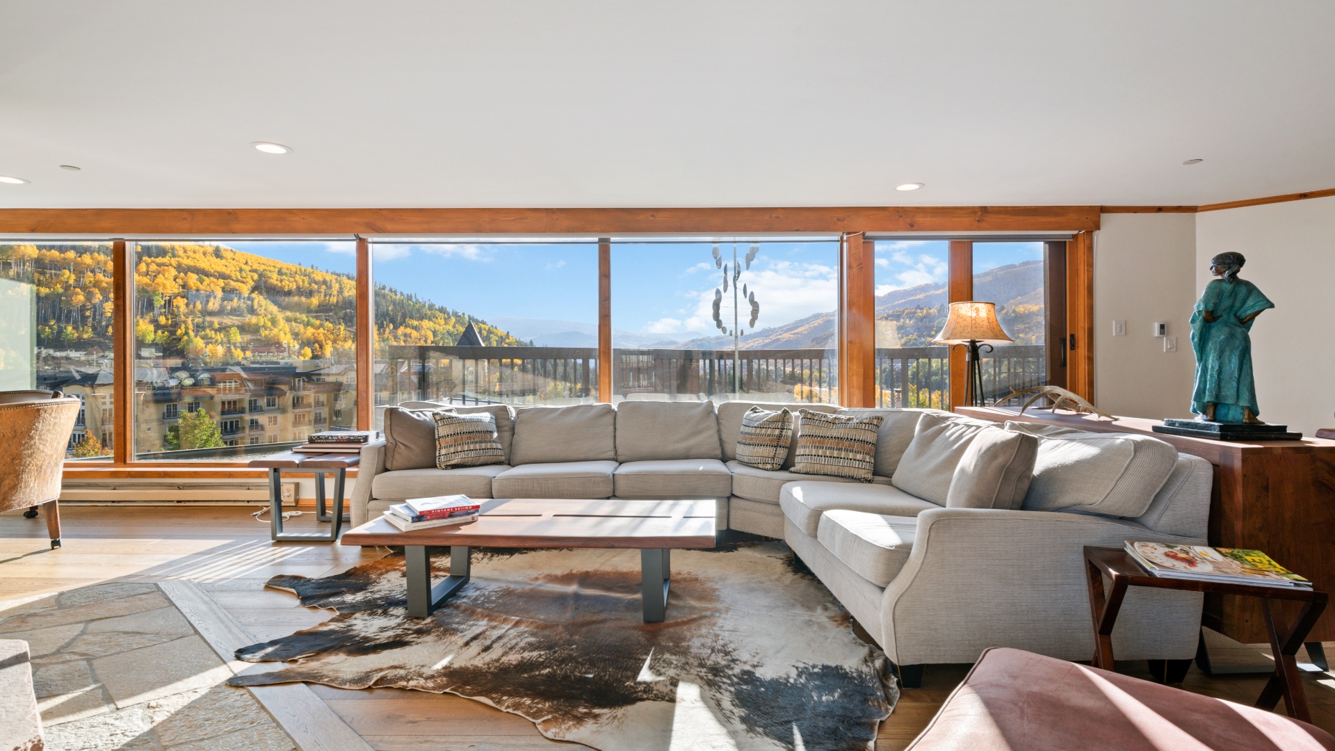 A luxurious living room with a large couch and windows looking out to fall foliage at a condo at Vai 