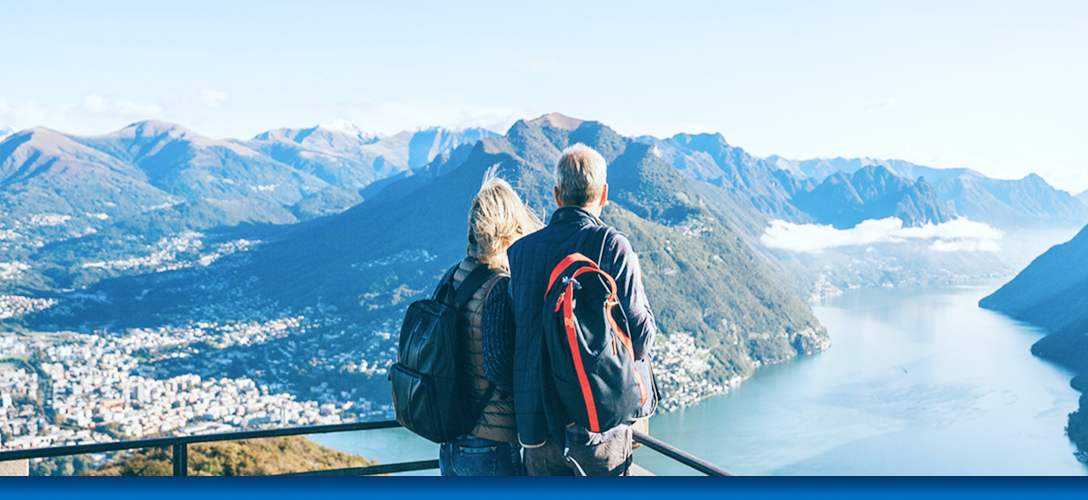 A couple standing at a lookout point and admiring the gorgeous mountains and lake in front of them.