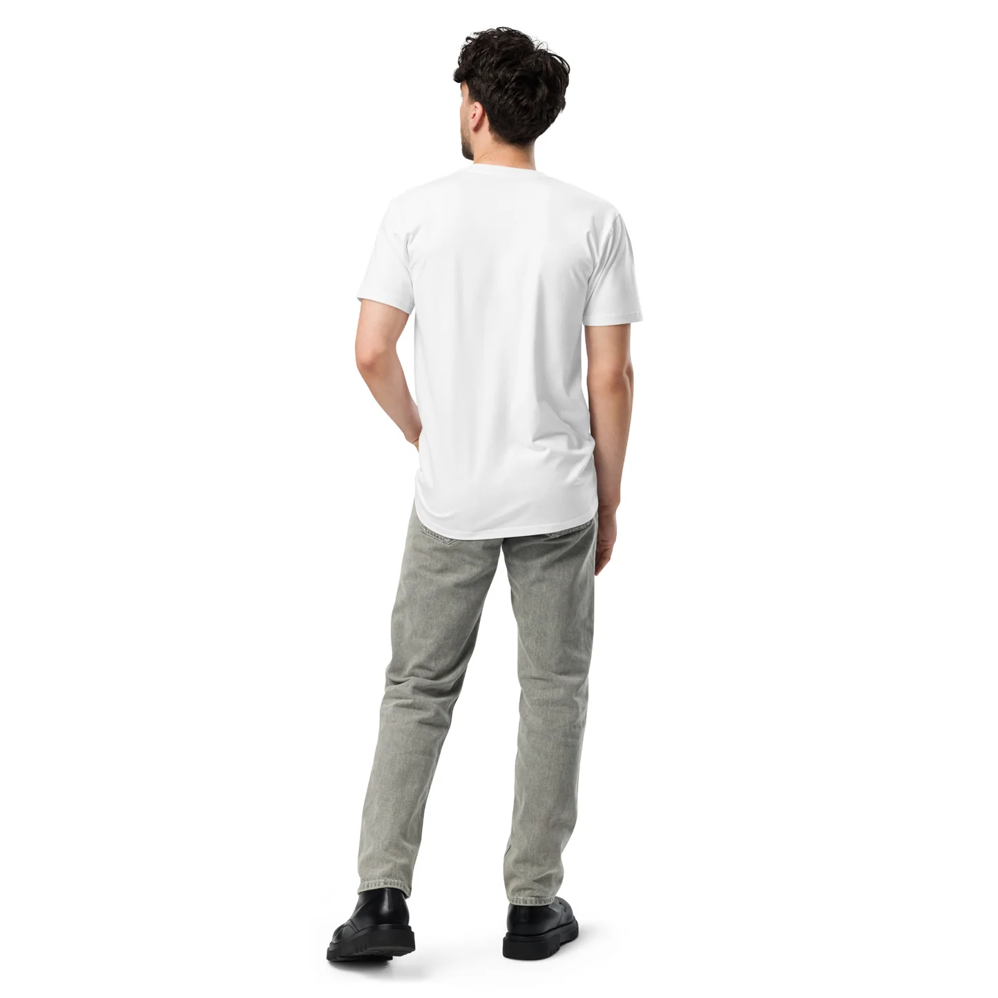 A man viewed from the back stands against a plain white background. He is wearing a white t-shirt, grey jeans, and black boots. His left hand is tucked into his jeans pocket, and his right arm hangs loosely at his side. The image appears to be a product mockup.