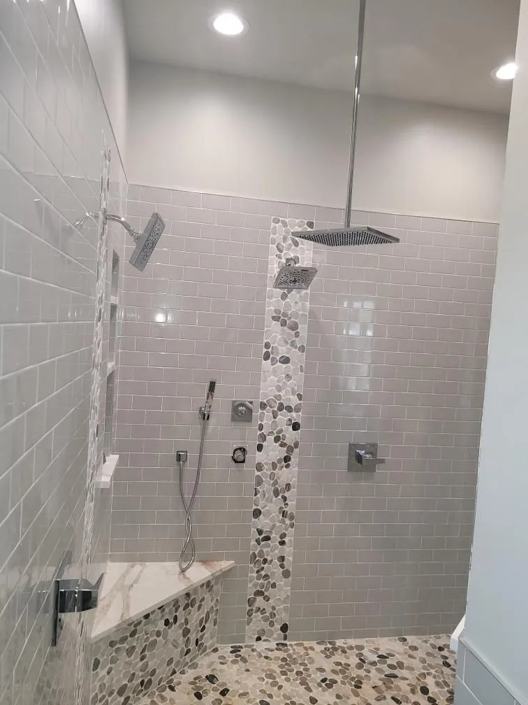 Custom walk-in shower with rainfall showerhead, handheld sprayer, tiled bench, and decorative stone accents showcases premium plumbing installation, luxury bathroom remodeling, and modern residential shower design with comfort.