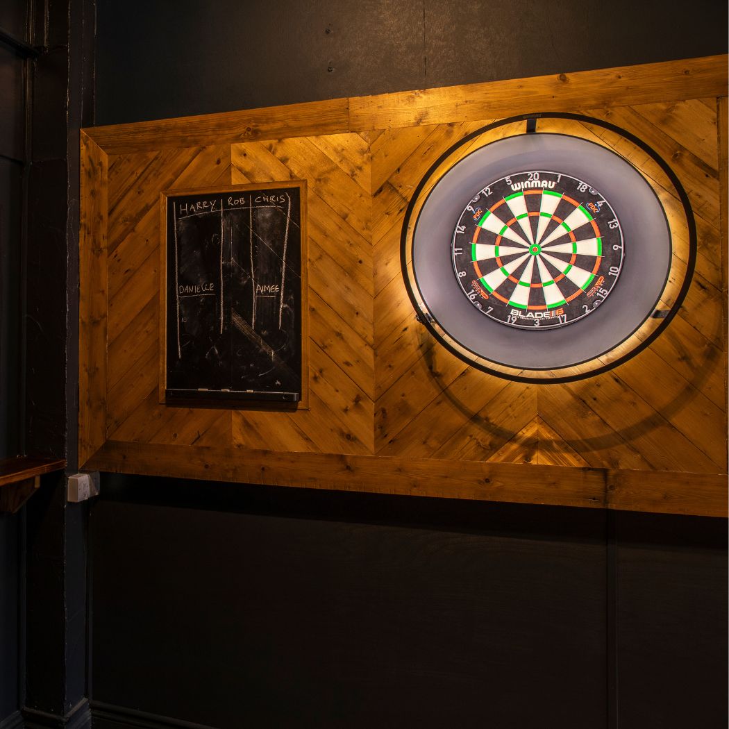 A dedicated darts area at The Arrow with dartboards, a scoring board and wooden panelled backdrop, designed for casual games and social visits.