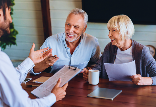 An elderly couple speaking to an advisor while reviewing papers at a table.