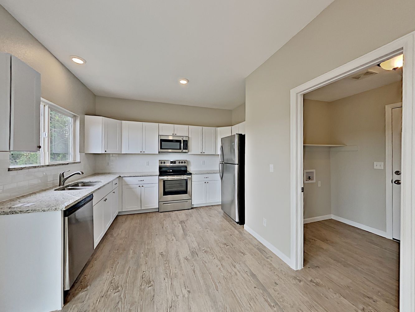 Beautiful kitchen with white cabinets, stain-less steel appliances and updated wood-style flooring at Invitation Homes Denver.