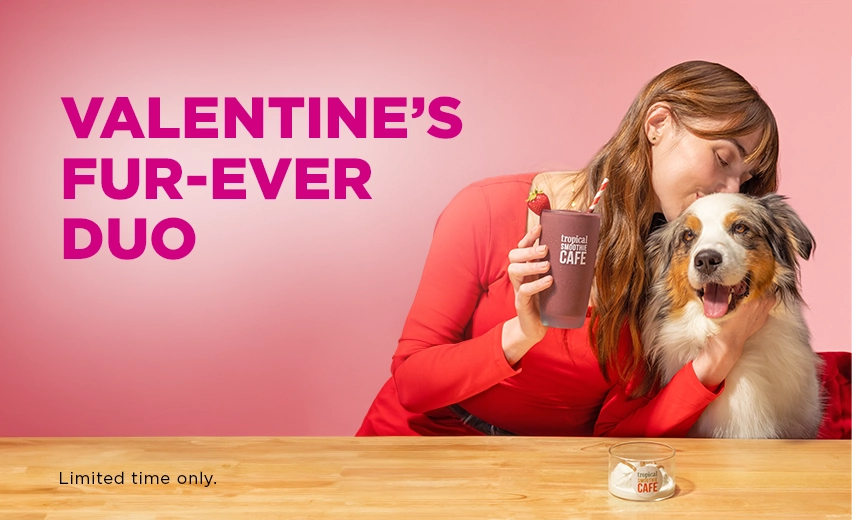 Valentine’s Fur-Ever Duo at Tropical Smoothie Cafe featuring a woman holding a limited time Chocolate Covered Strawberry Smoothie next to her dog, highlighting the limited time Puppy Power Bowl.