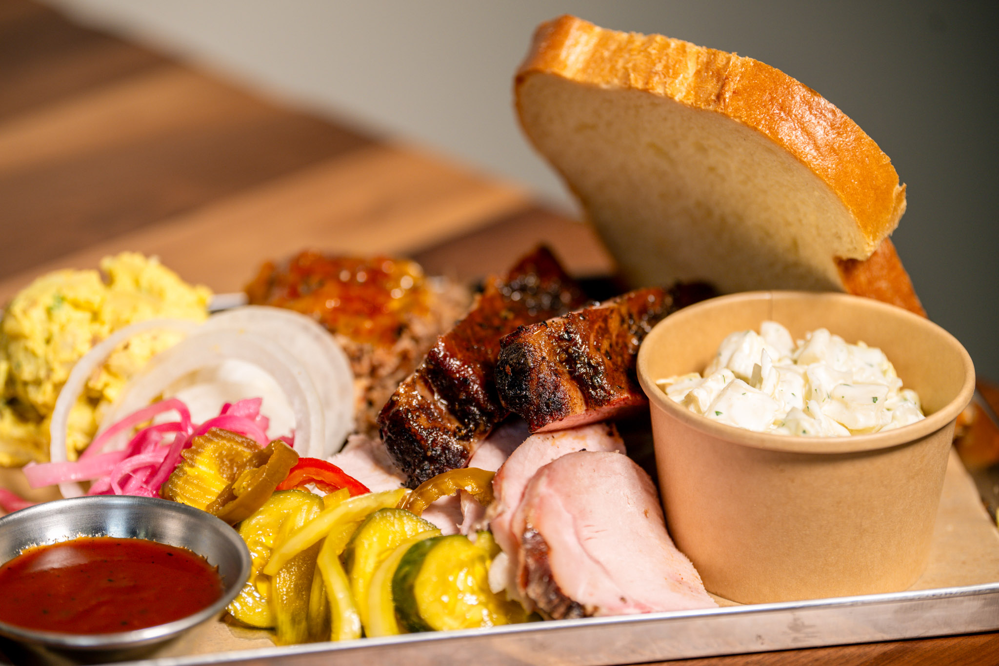 The Farmers Trinity — Brisket, Spareribs, and Jalapeño Cheddar Beef Sausage — served with mustard potato salad, coleslaw, pickled red onions, bread and butter pickles, pickled peppers, Joe's BBQ sauce, and white bread.