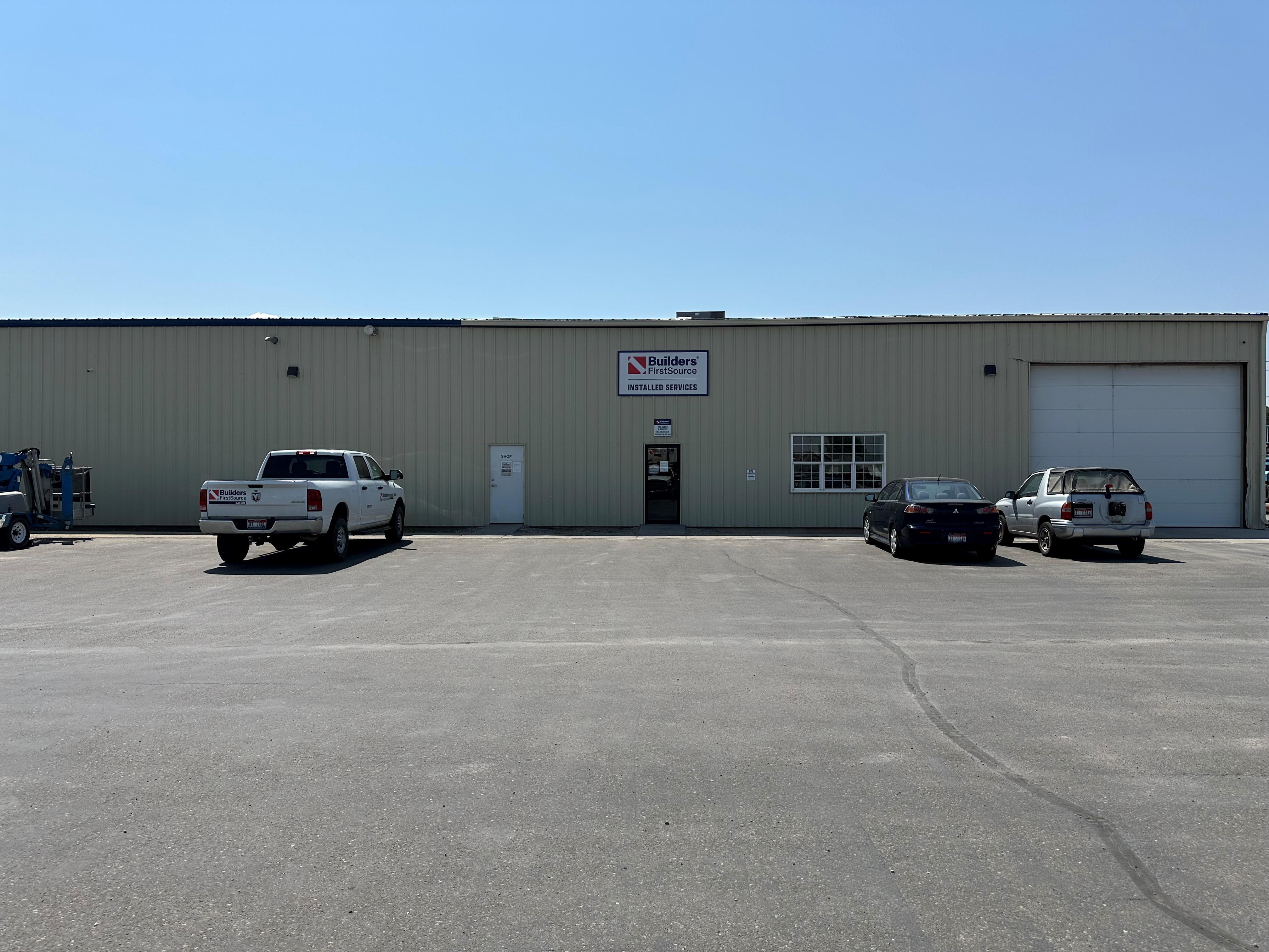 A Builders FirstSource facility in Idaho Falls, specialized in window and garage door installation services, with a parking lot in front featuring a white company truck and two other vehicles.