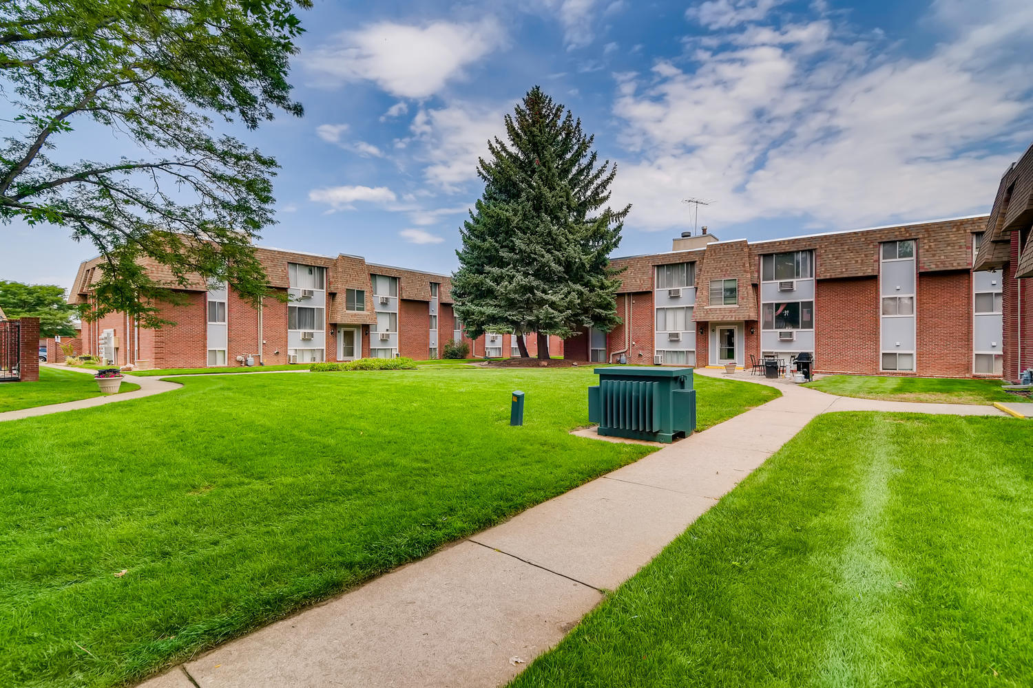 Grassy lawn with trees, sidewalk, and brick and siding building exterior.