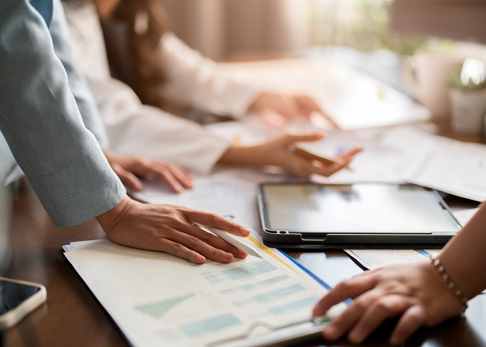 Close-up of hands reviewing financial charts and documents with a tablet on a desk.