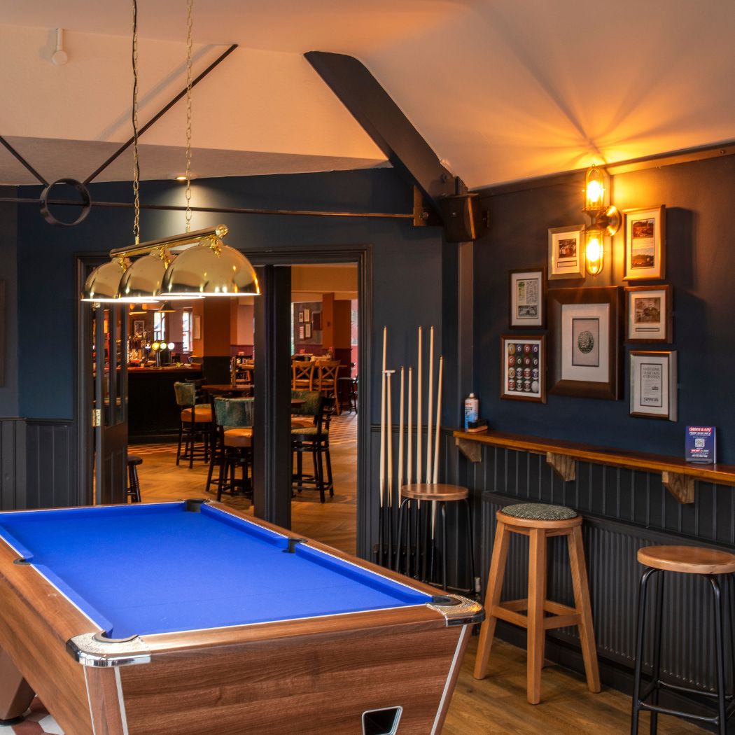 Pool table area inside The Arrow featuring a full-size table, surrounding seating and overhead lighting, offering a space for games and socialising.